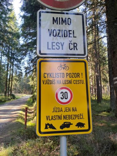Dopravní značka s upozorněním pro cyklisty, že v lese jsou stromy, nákladní auta prasata