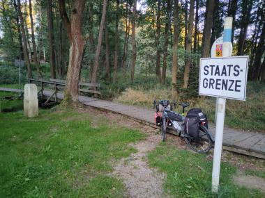 Kolo postavené u dřevěné lávky přes bažinatou louku (teď vyschlou), v popředí značka Pozor státní hranice (německy)