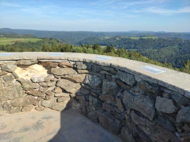 Kamenná zídka zábradlí s tabulkami o tom co je kde vidět, za ní pohled do kraje na lesy a kopce v okolí